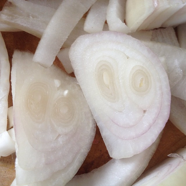 Sliced onion halves with concentric rings resembling smiling faces, surrounded by chopped onion pieces on a wooden cutting board.
