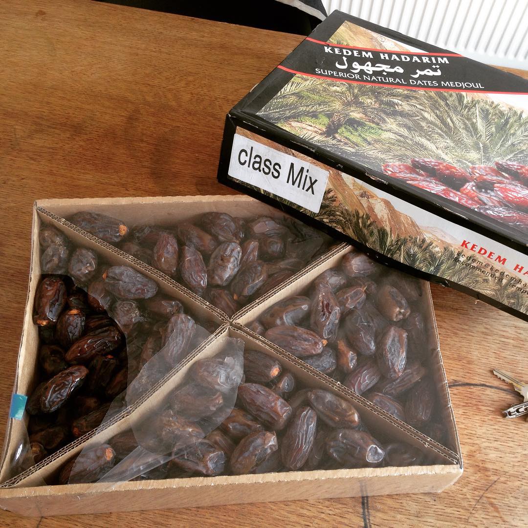 Open box of Medjool dates divided into four sections on a wooden table, with the box lid labeled "class Mix" beside it.