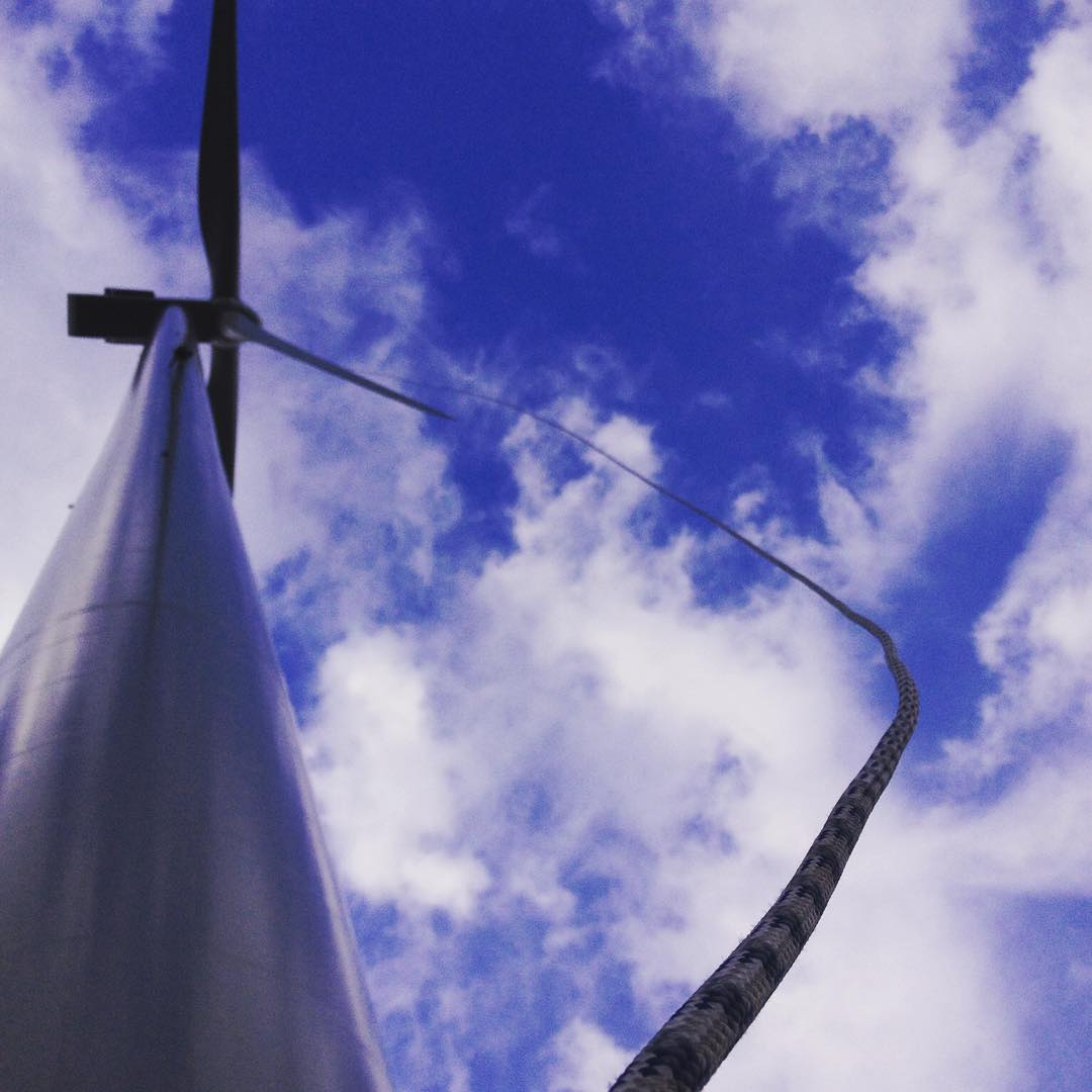 Low-angle view of a wind turbine against a blue sky with clouds, with a rope hanging in the foreground.