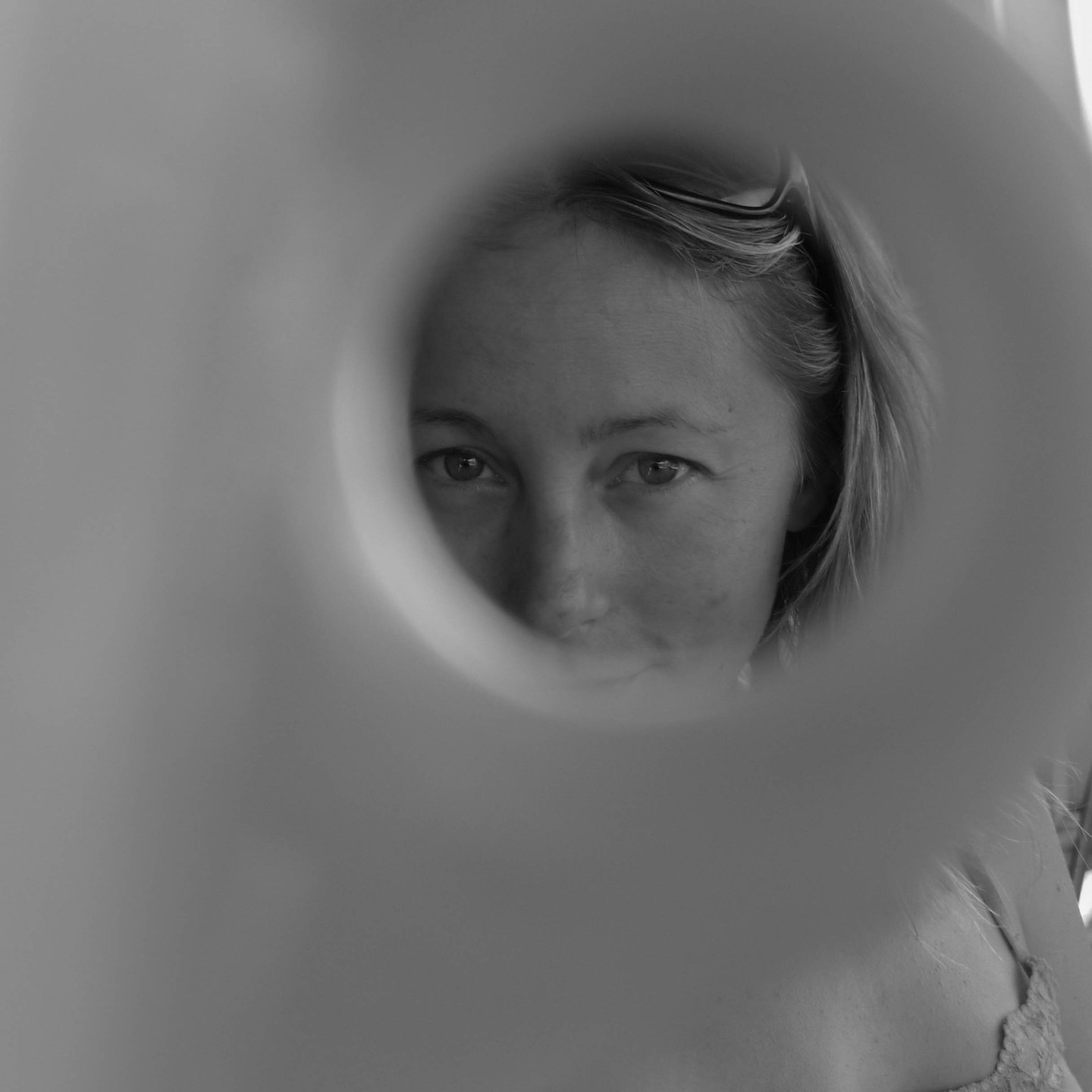 Black and white photo of a woman's face seen through a circular opening, with hair pushed back, in soft focus surroundings.