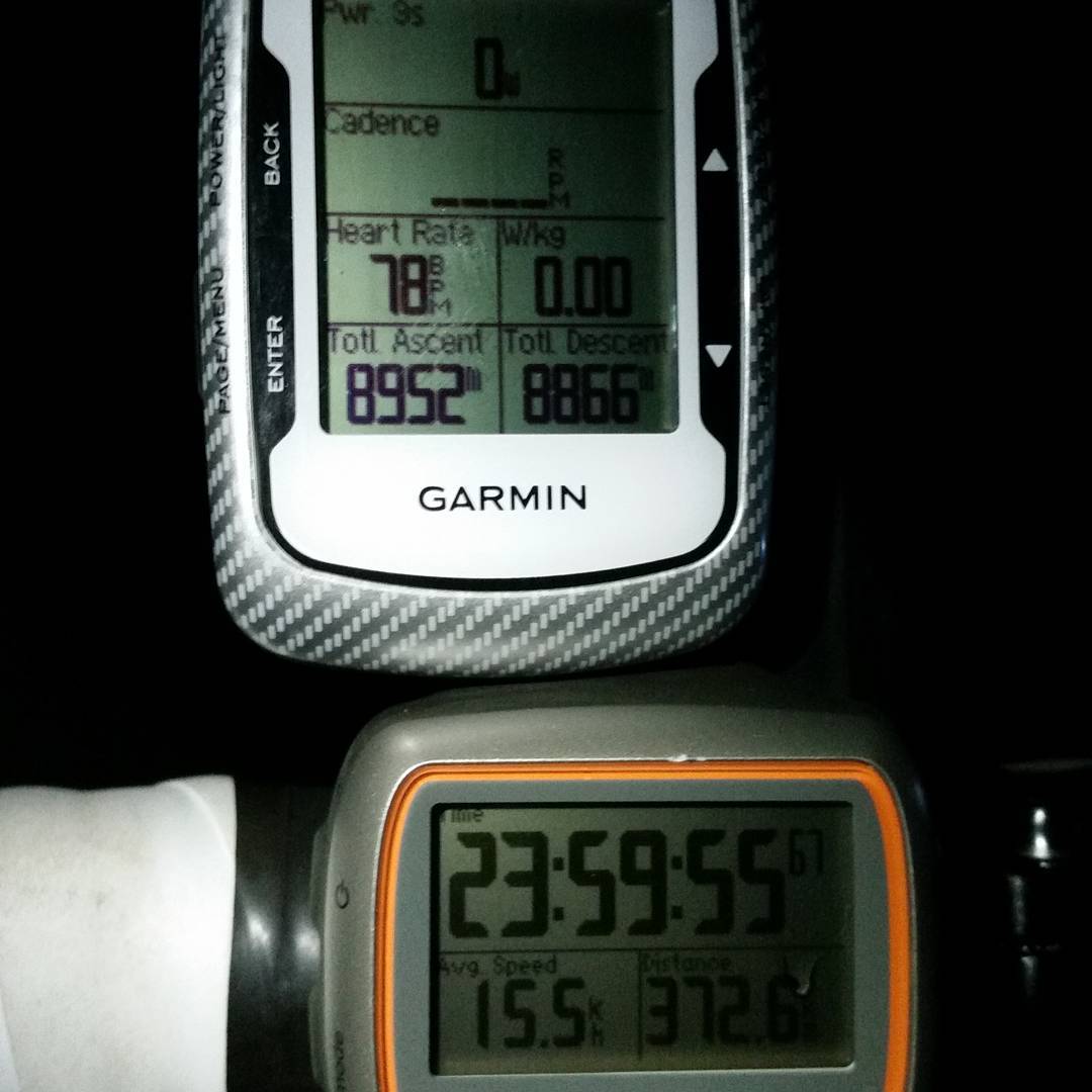 Two cycling computers, a Garmin and an orange-trimmed GPS device, showing ride data including heart rate, ascent, time, and distance.