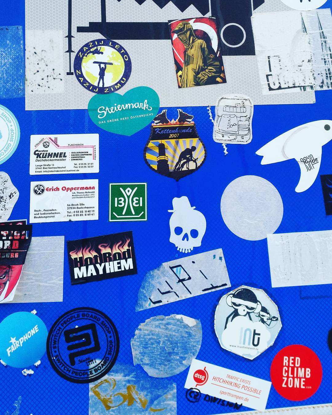 Blue surface covered with numerous stickers including logos, business cards, a skull, and various brand designs.