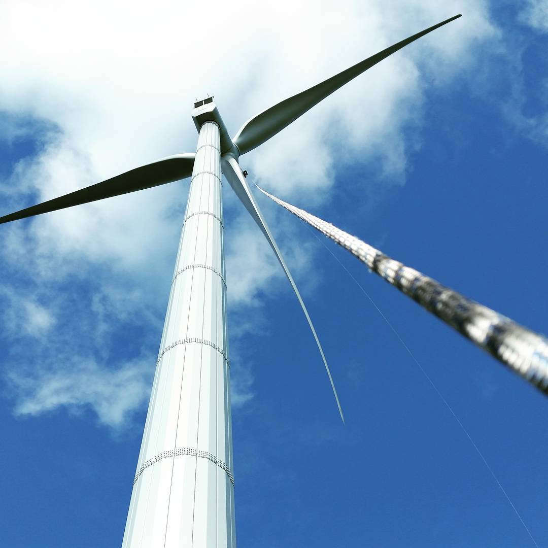 Upward view of a wind turbine tower and blades against a blue sky with scattered white clouds.