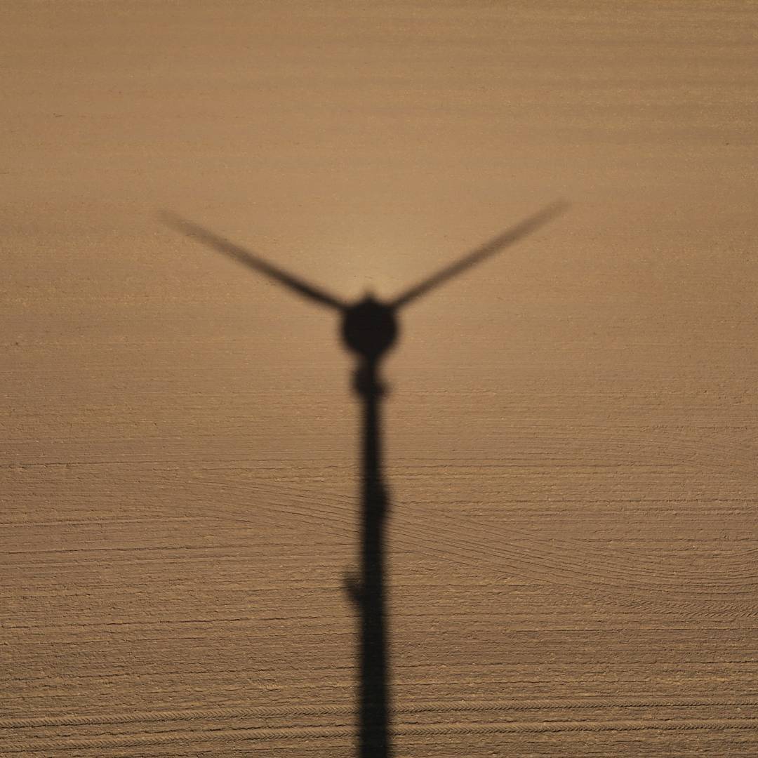 Silhouette shadow of a wind turbine cast on a plowed field, viewed from above at low sun angle.