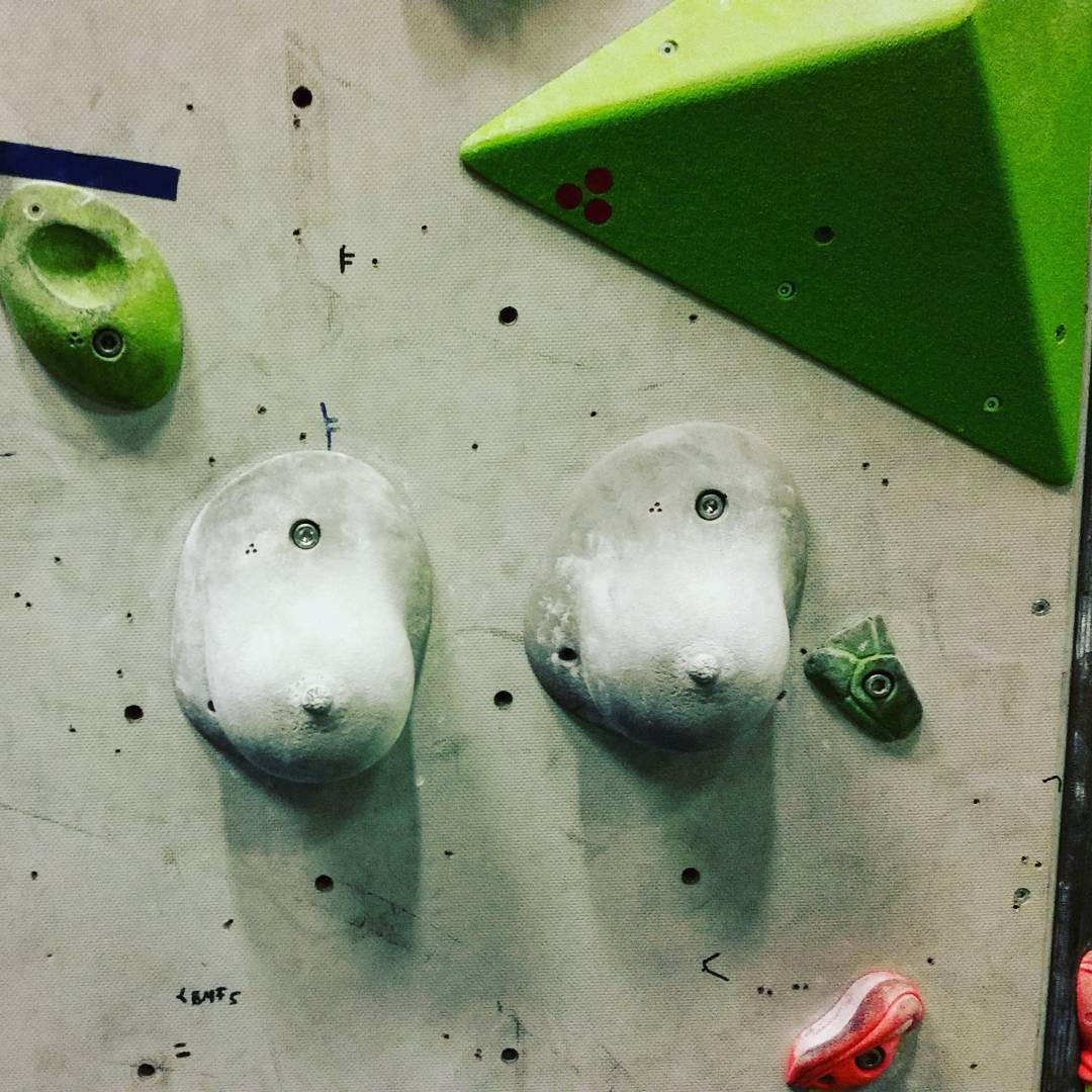Climbing wall with two large chalky white holds, a green triangular hold, and a small green hold with bolt.