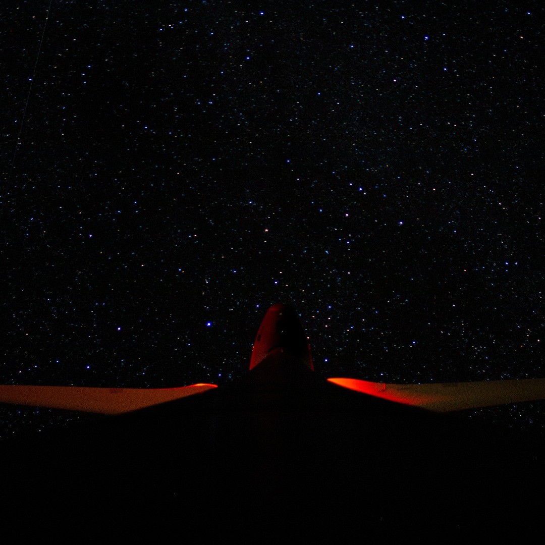 Silhouette of an aircraft's tail and wings lit red against a night sky filled with stars.