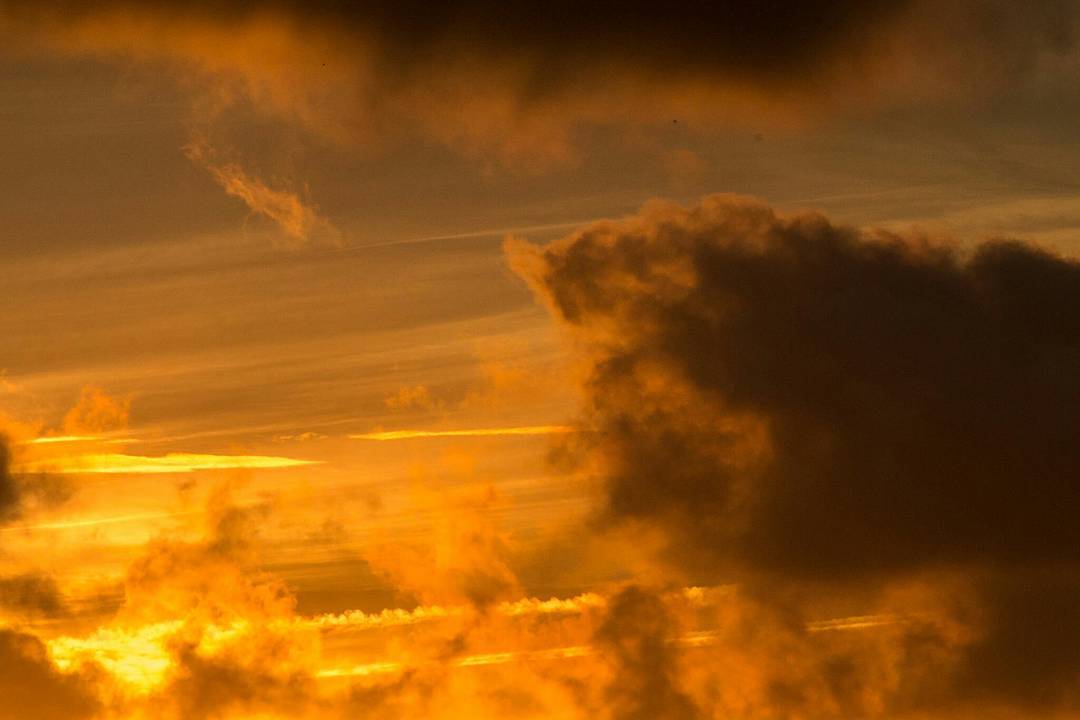 Dramatic sunrise sky with dark storm clouds silhouetted against glowing orange and gold light, thin cloud streaks visible.