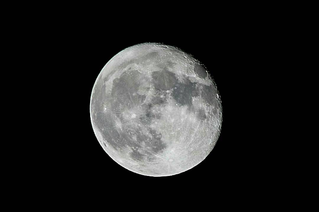 Close-up photograph of the moon against a black night sky, showing cratered surface texture and grey tonal variations.
