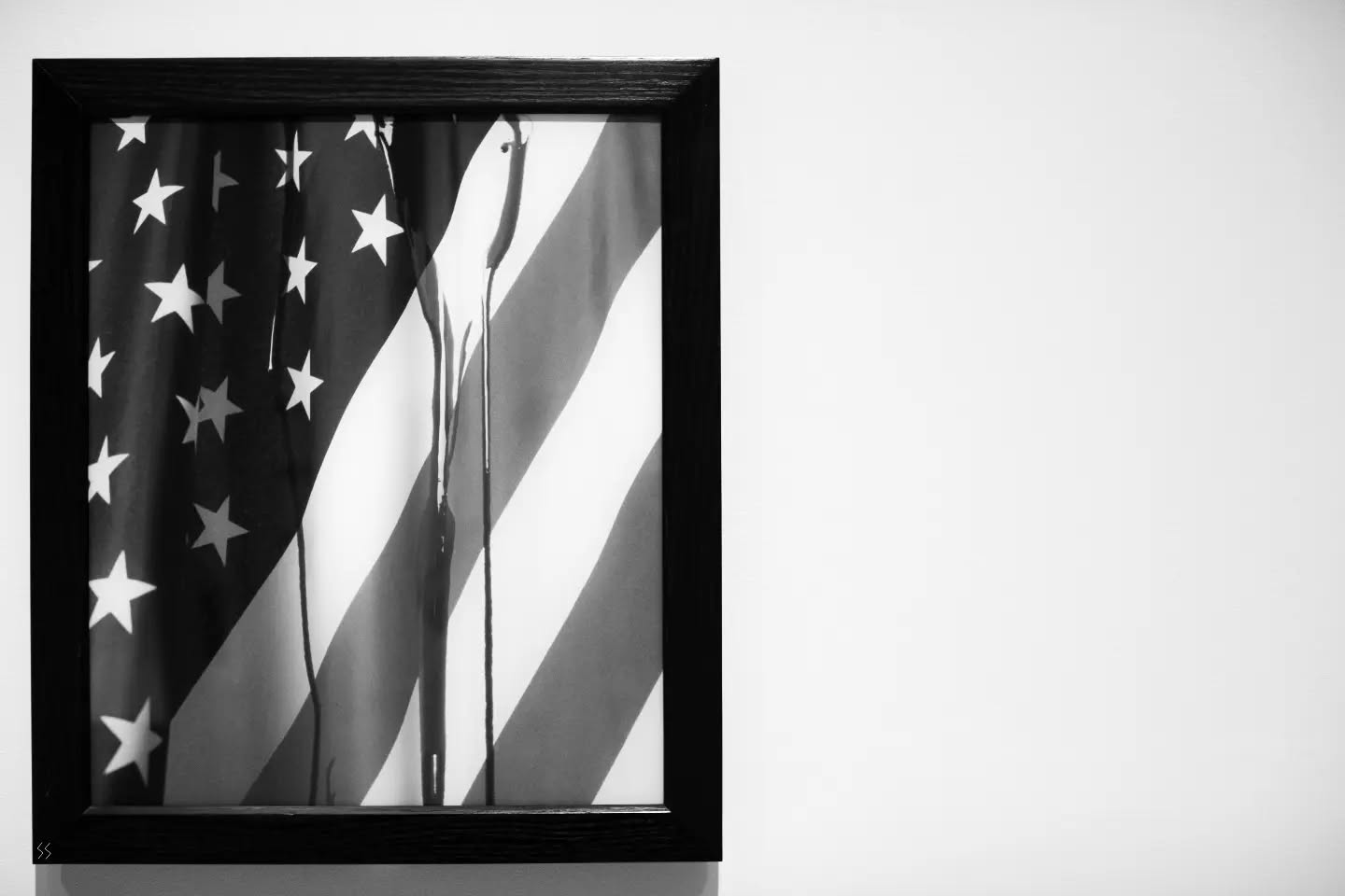 Black-and-white photo of a framed image showing an American flag with dark drips running vertically down it, in a black frame.