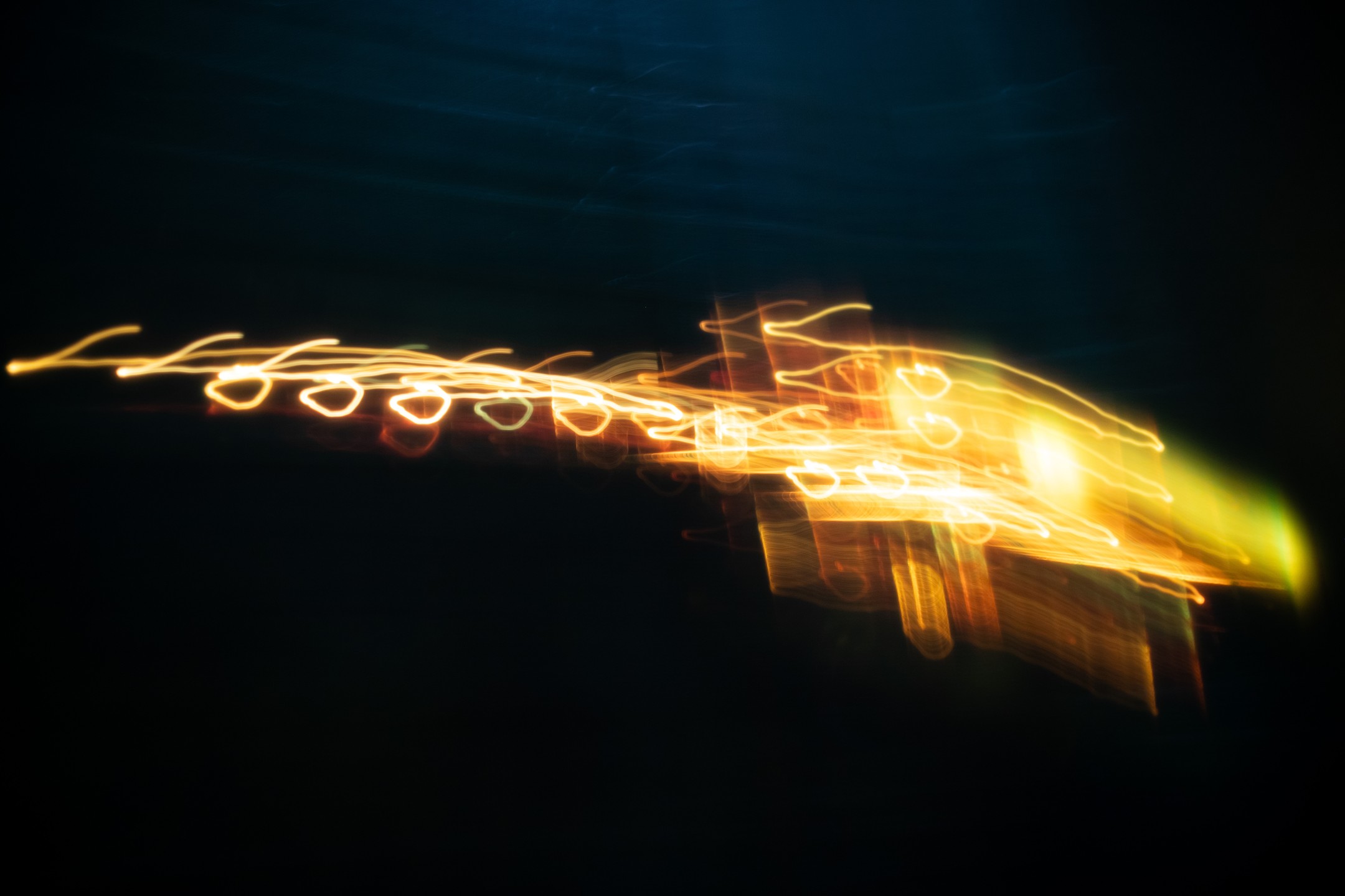 Long-exposure light trails in gold and amber forming loops and streaks against a dark background.