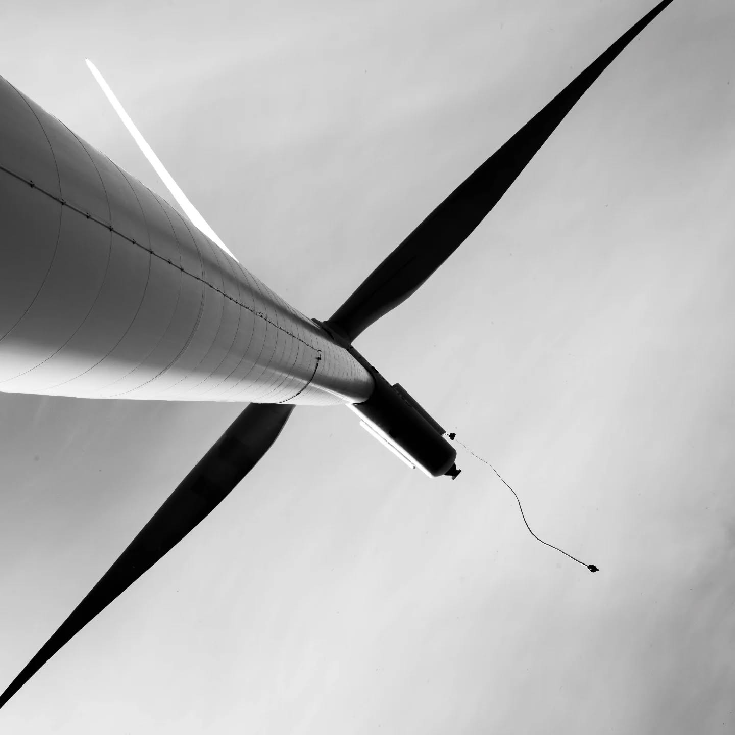 Black and white low-angle photo of a wind turbine, showing the nacelle and two blades against a plain sky.