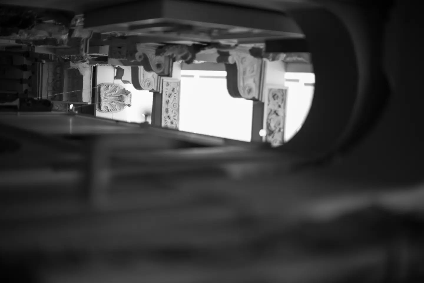 Black and white photo through a narrow gap, showing ornate carved architectural details and columns in soft focus.