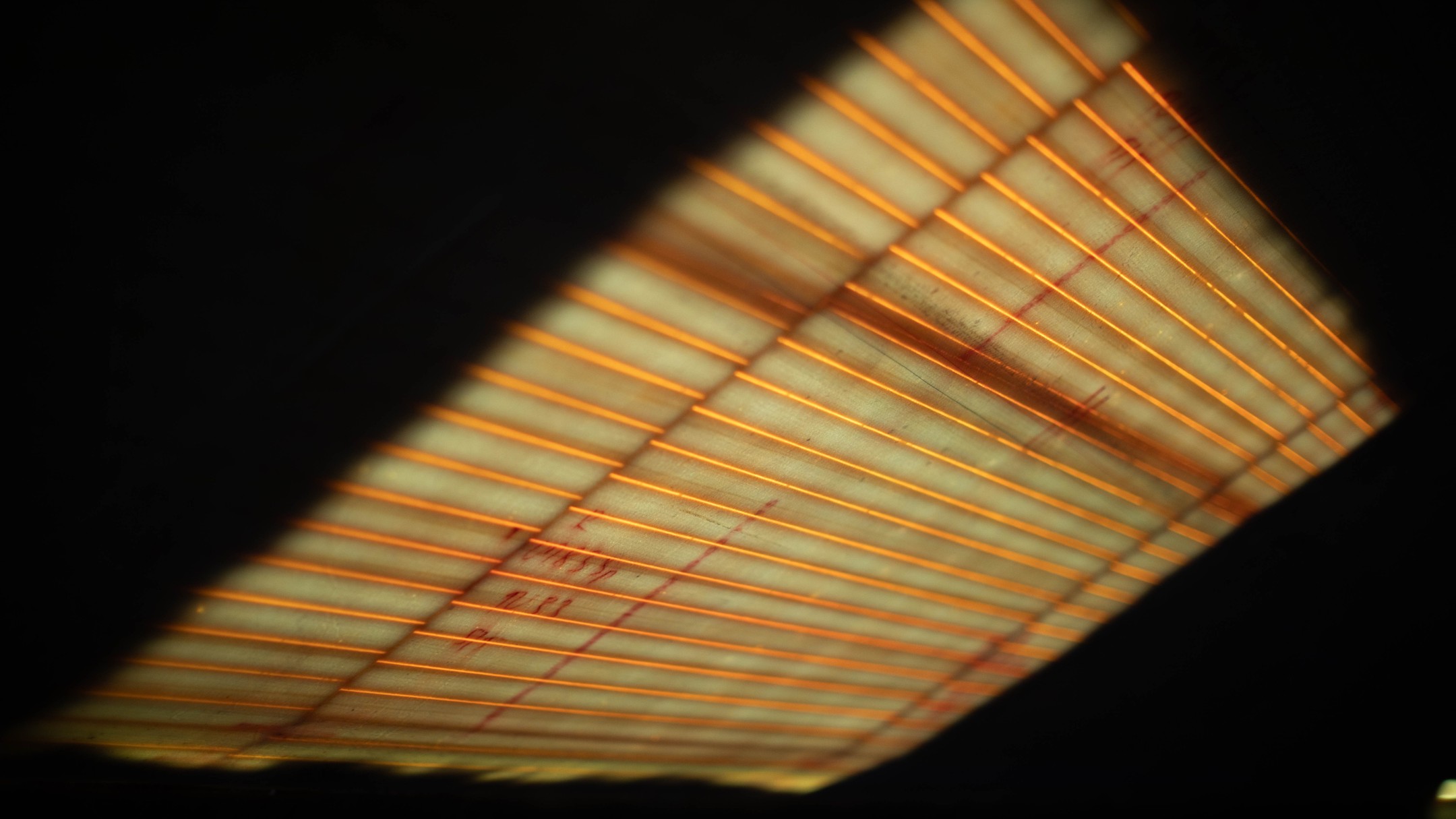 Close-up of a heating element's glowing orange coils against a beige panel with faint red pen marks, set in darkness.