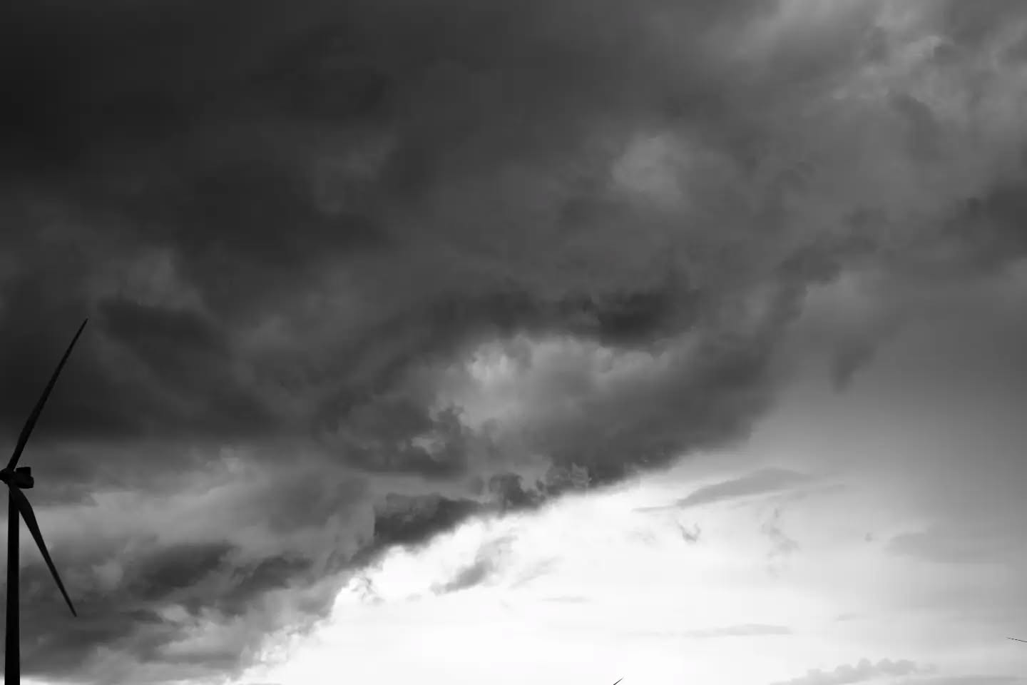 Black and white photo of a wind turbine silhouette against a dramatic, dark cloudy sky.