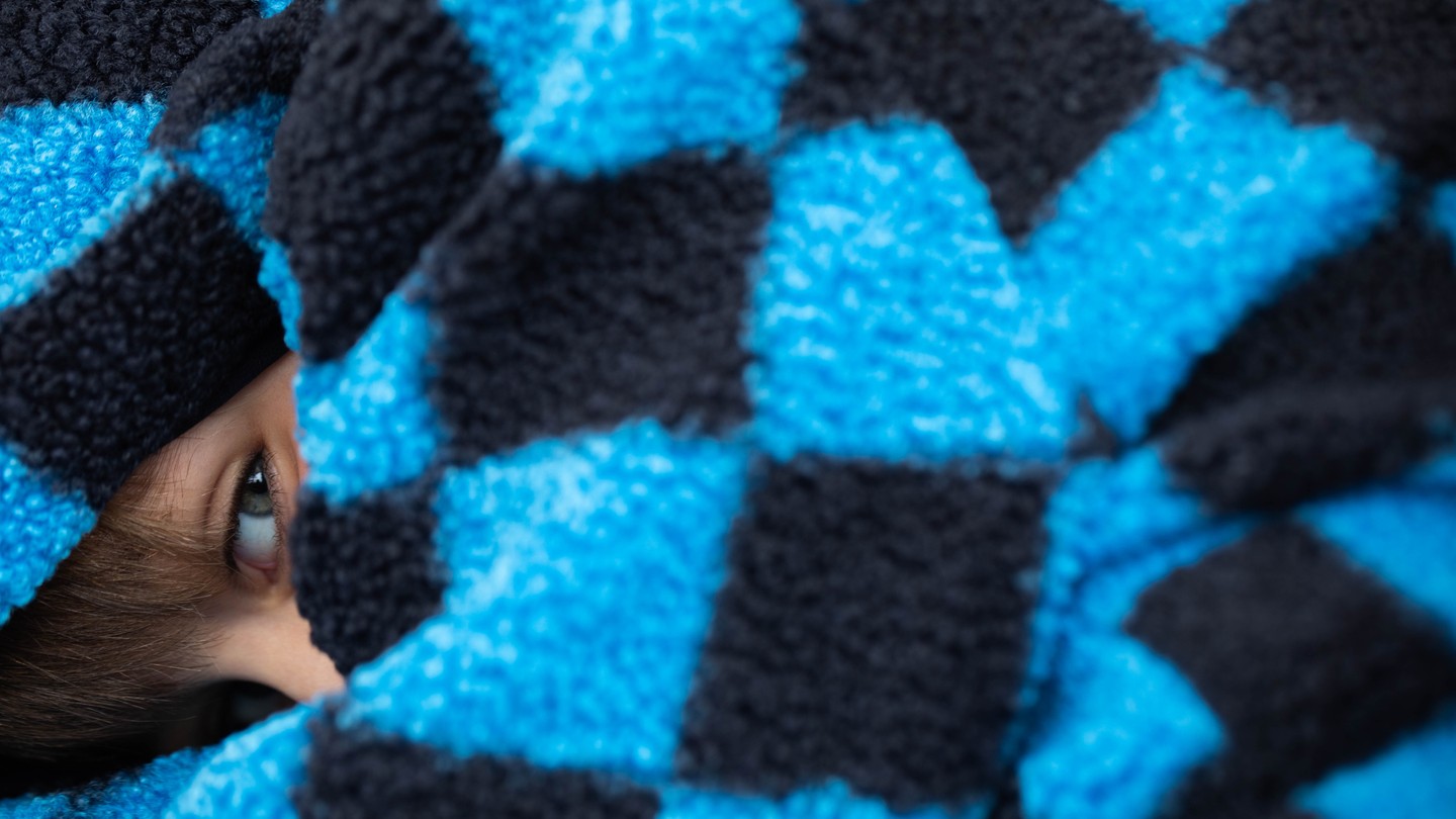 Child's eye peeking out from beneath a blue and black checkered fuzzy blanket.