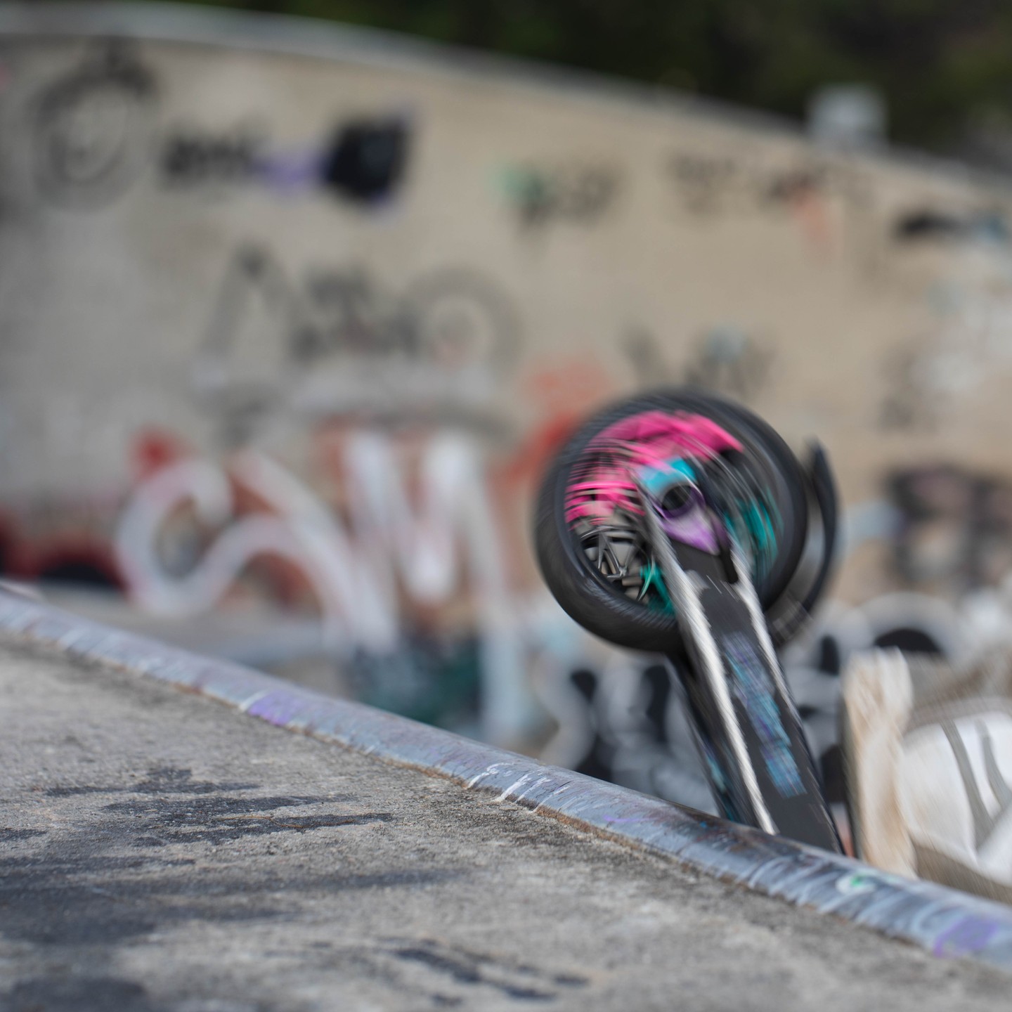 Blurred spinning skateboard wheel above a concrete ramp edge, with graffiti-covered wall in the background.