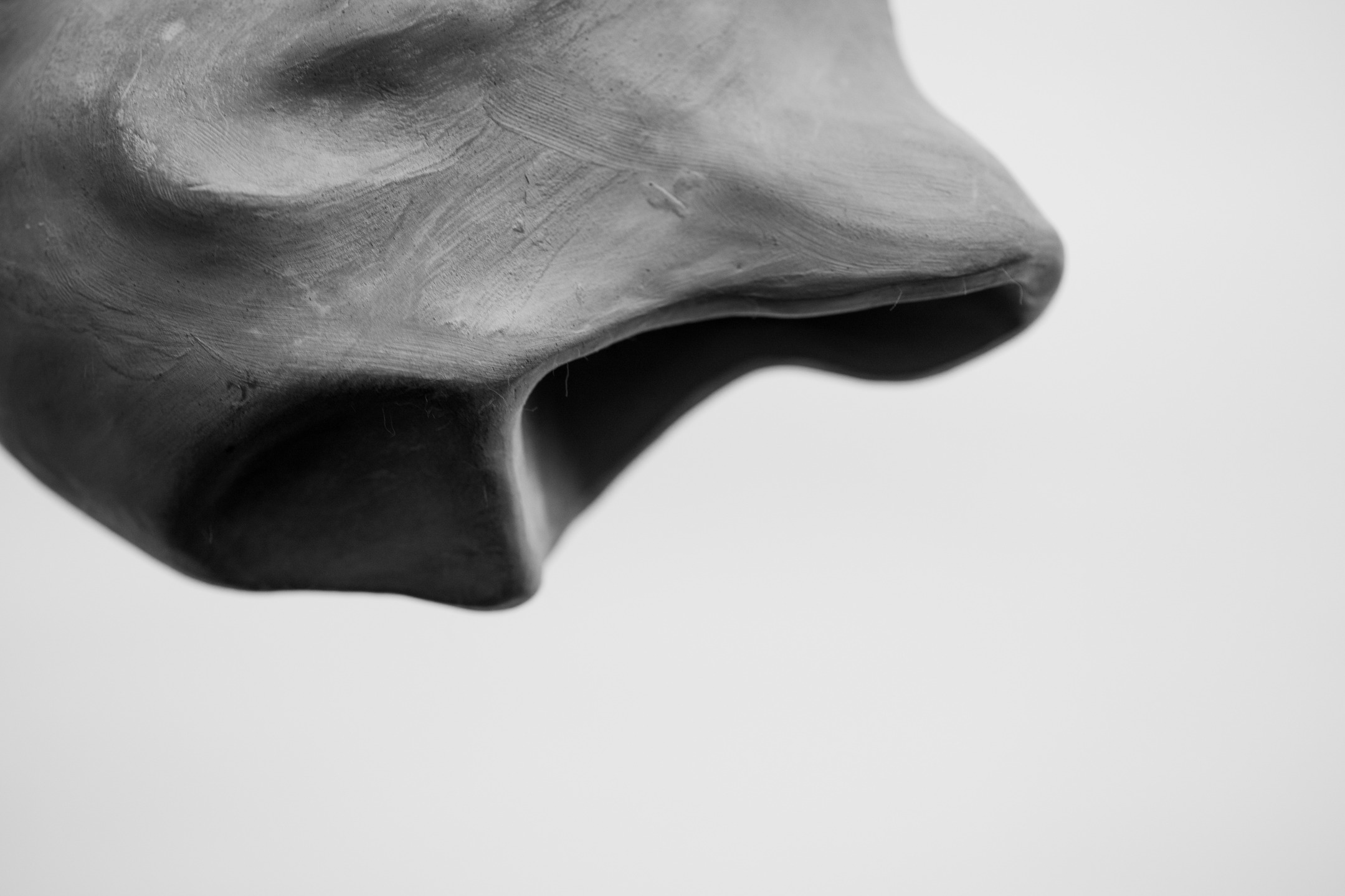 Close-up black-and-white photo of a smooth clay or plaster sculpture with two dark, hollow openings, against a plain light background.