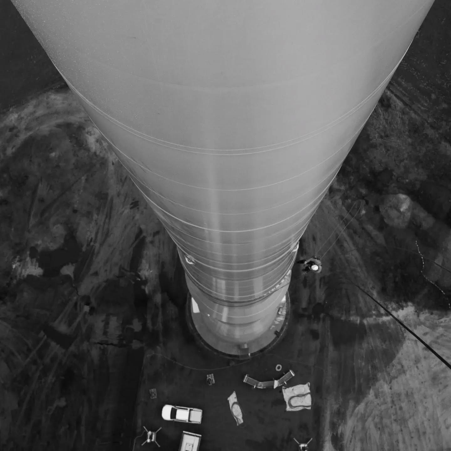 Aerial view looking straight down a wind turbine tower base, with a car and equipment on the ground beside it.