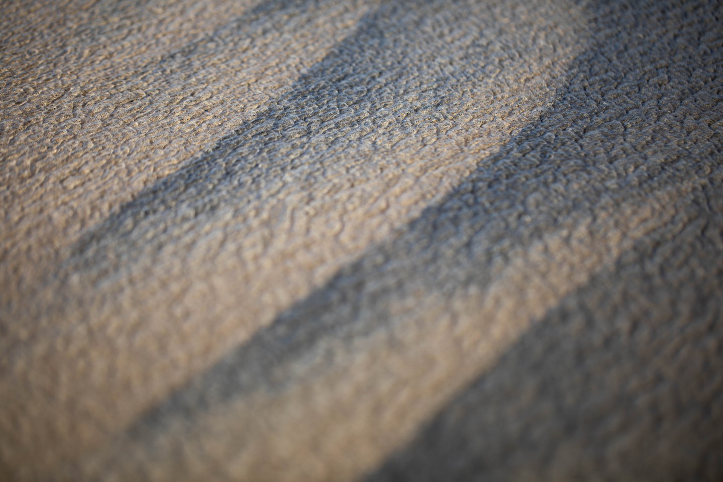 Close-up of a textured woven fabric surface with diagonal shadow bands crossing it.