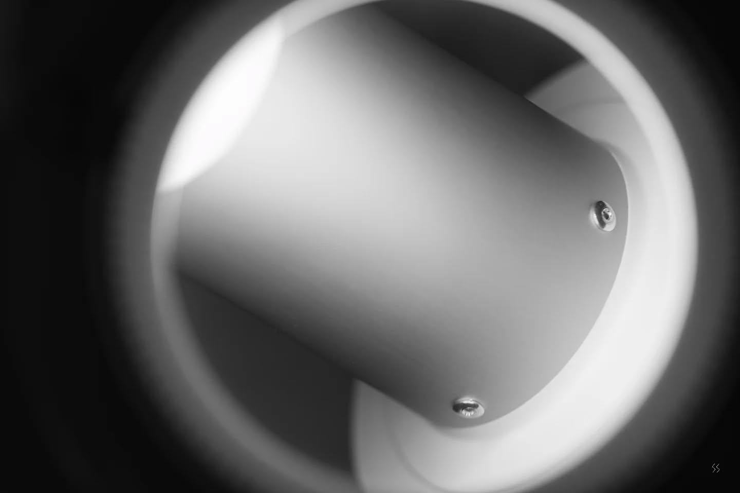 Black-and-white close-up of a cylindrical white object with two visible screws, set within a round opening, soft lighting and shadow.