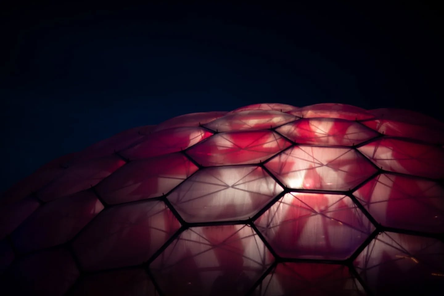 Geodesic dome with hexagonal panels illuminated in red and white light against a dark night sky.