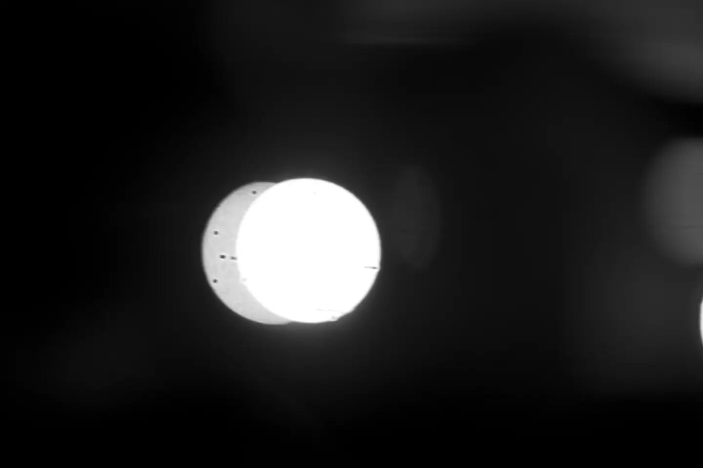 Black and white image of a bright glowing sphere overlapping a dimmer circular shape against a dark background.
