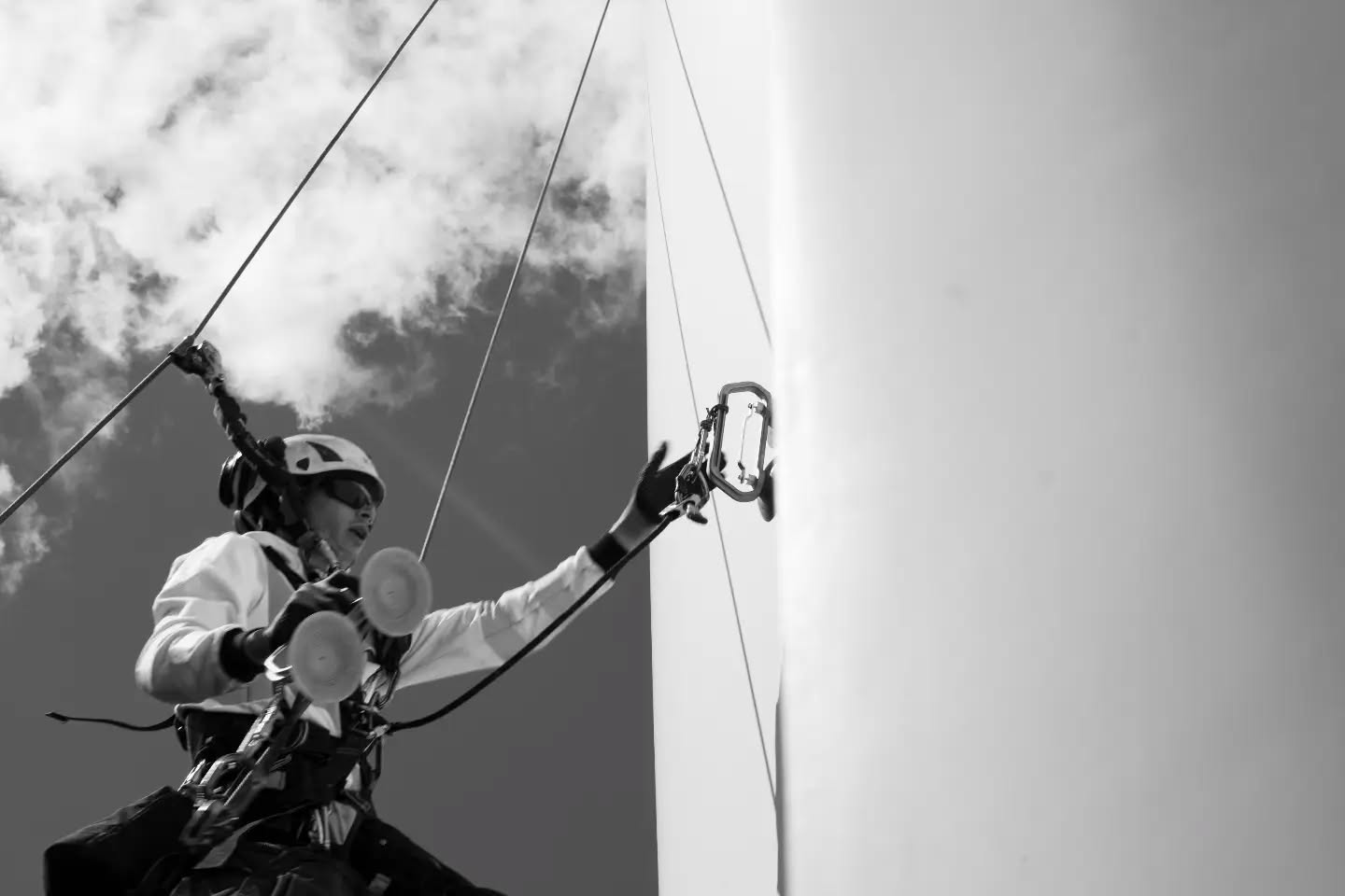 Black and white photograph of a person using rope access equipment, hands gripping the rope.