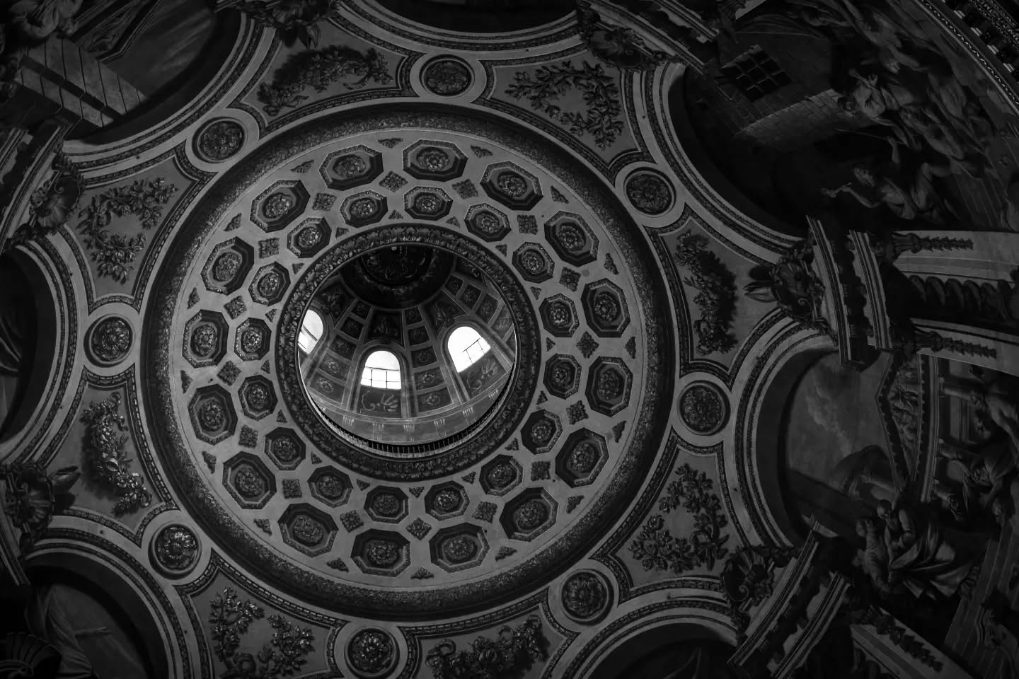Black-and-white photo of an ornate domed ceiling with concentric coffered rings, floral rosettes, and a central lantern with windows.