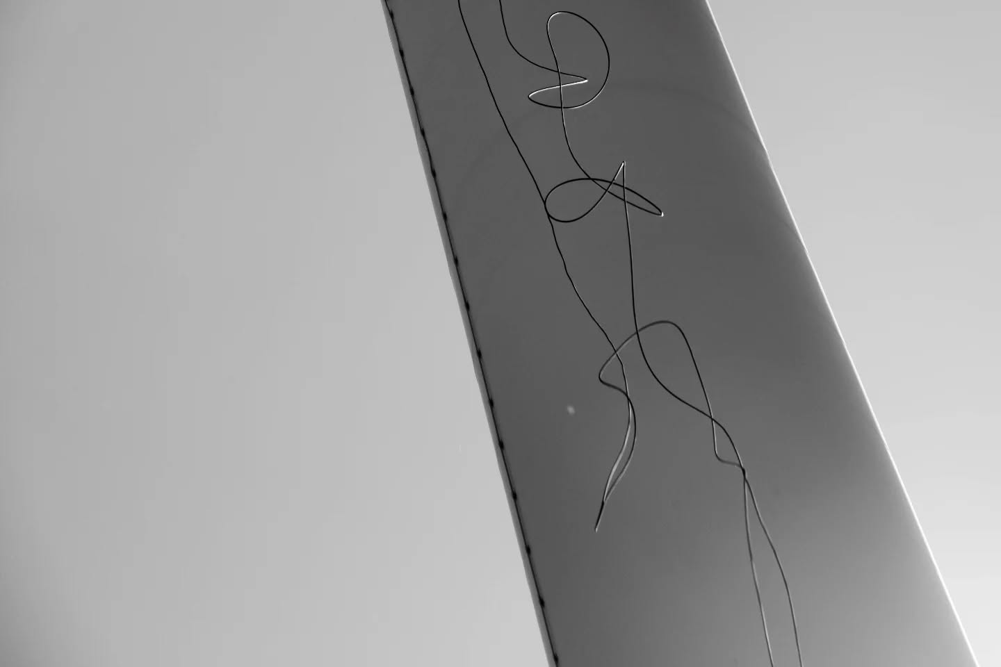 Black and white photo of a reflective diagonal surface with a tangled loop of thin wire or thread across it.