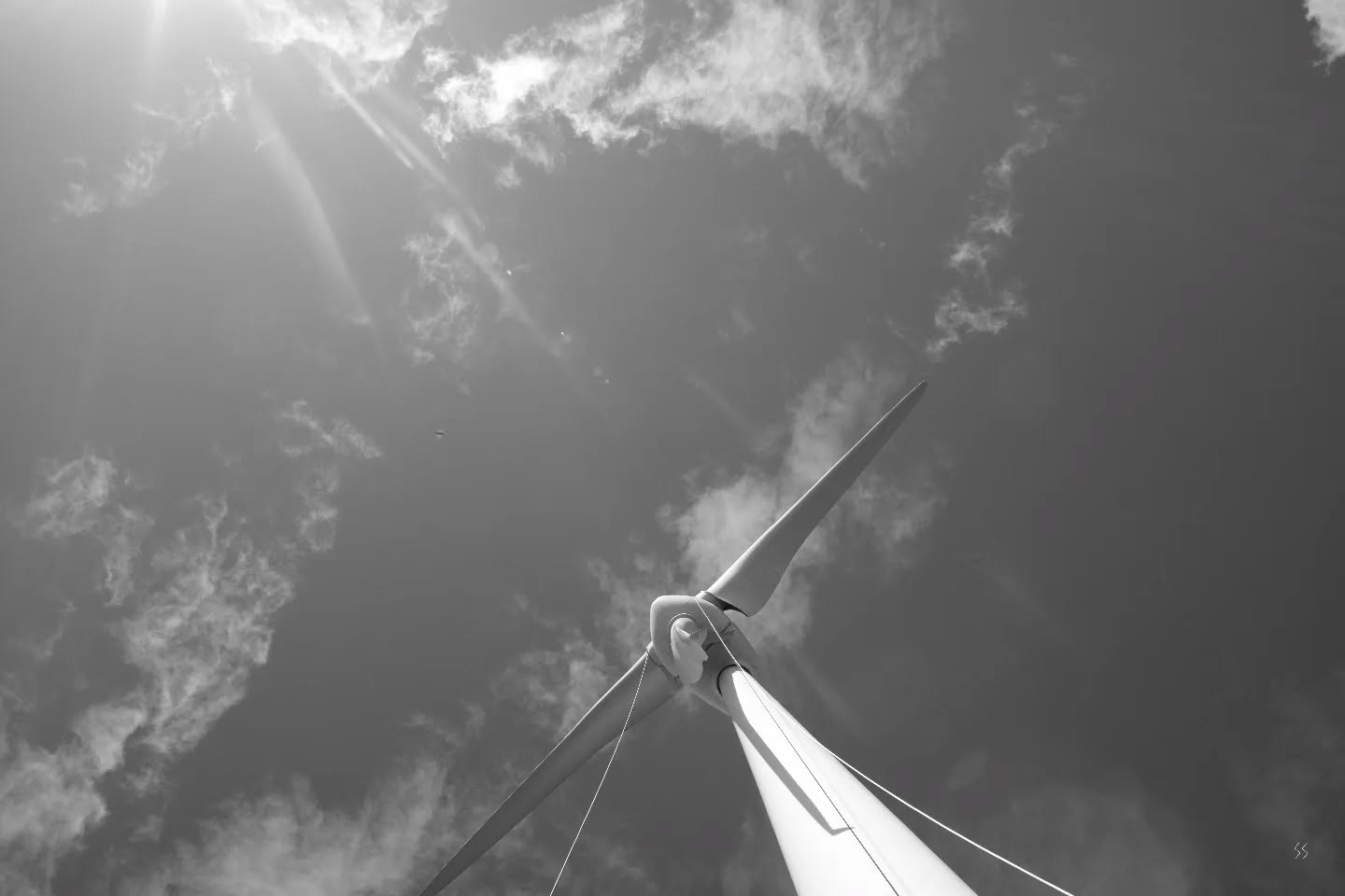 Black and white photo of a wind turbine's blades and hub viewed from below against a cloudy sky.