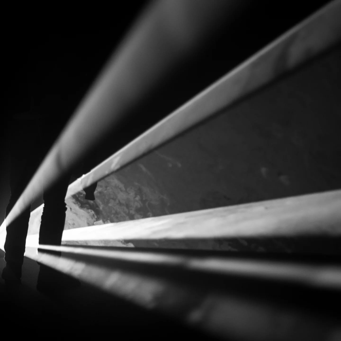 Black and white photo of a beam of light cutting through a dark room, with a silhouetted figure standing at its edge.