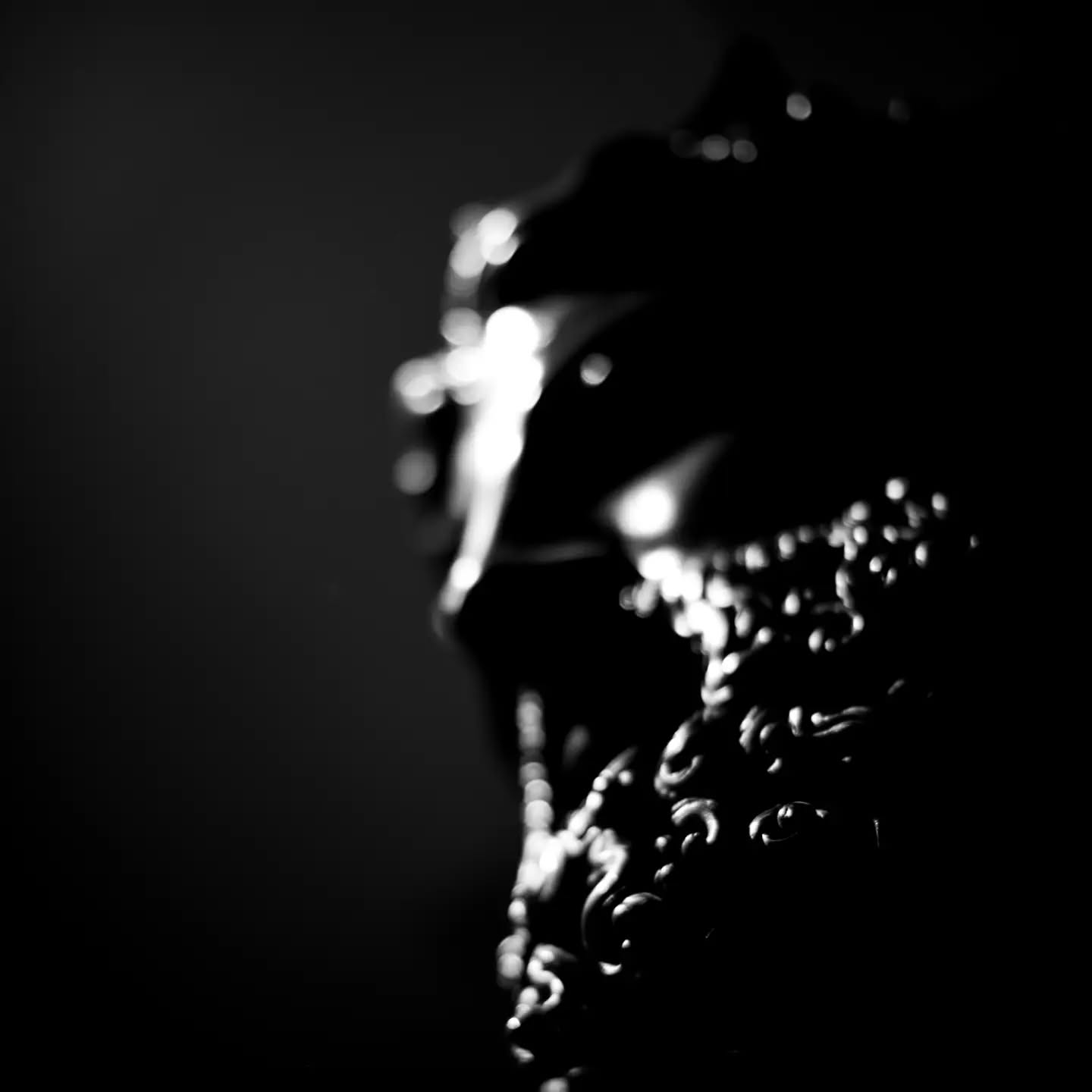 Black-and-white close-up of an ornately carved object with intricate scrollwork, edges catching light against a dark, out-of-