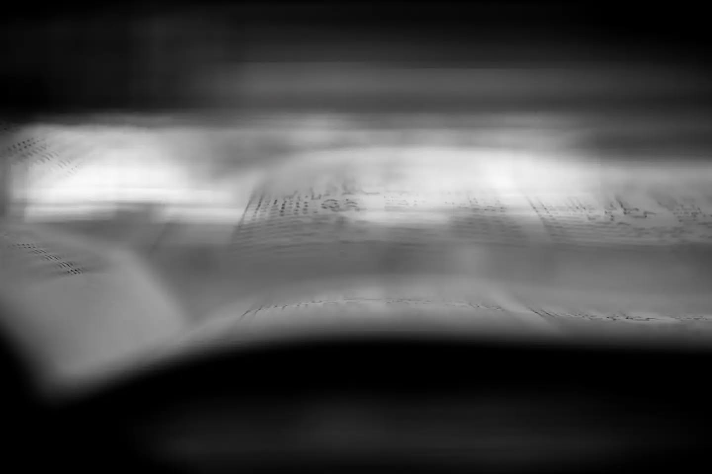 Blurred black-and-white photo of an open book with text, motion blur obscuring most details.