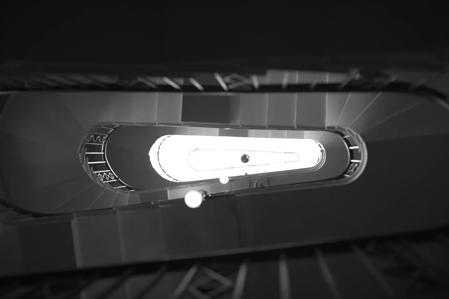 Black and white top-down view of a spiral staircase, looking down through its center toward a bright light at the bottom.