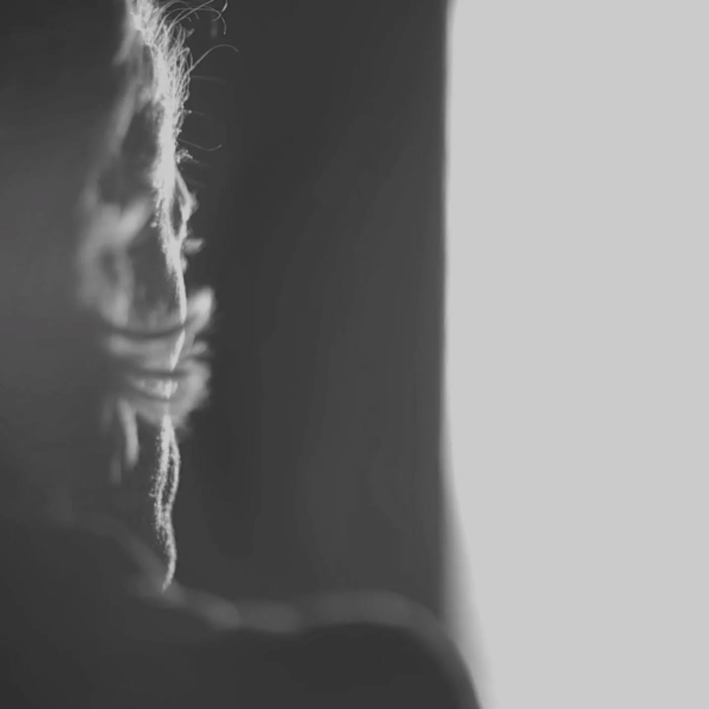 Black-and-white close-up profile of a person's face and hair in shadow against a plain light-gray background.