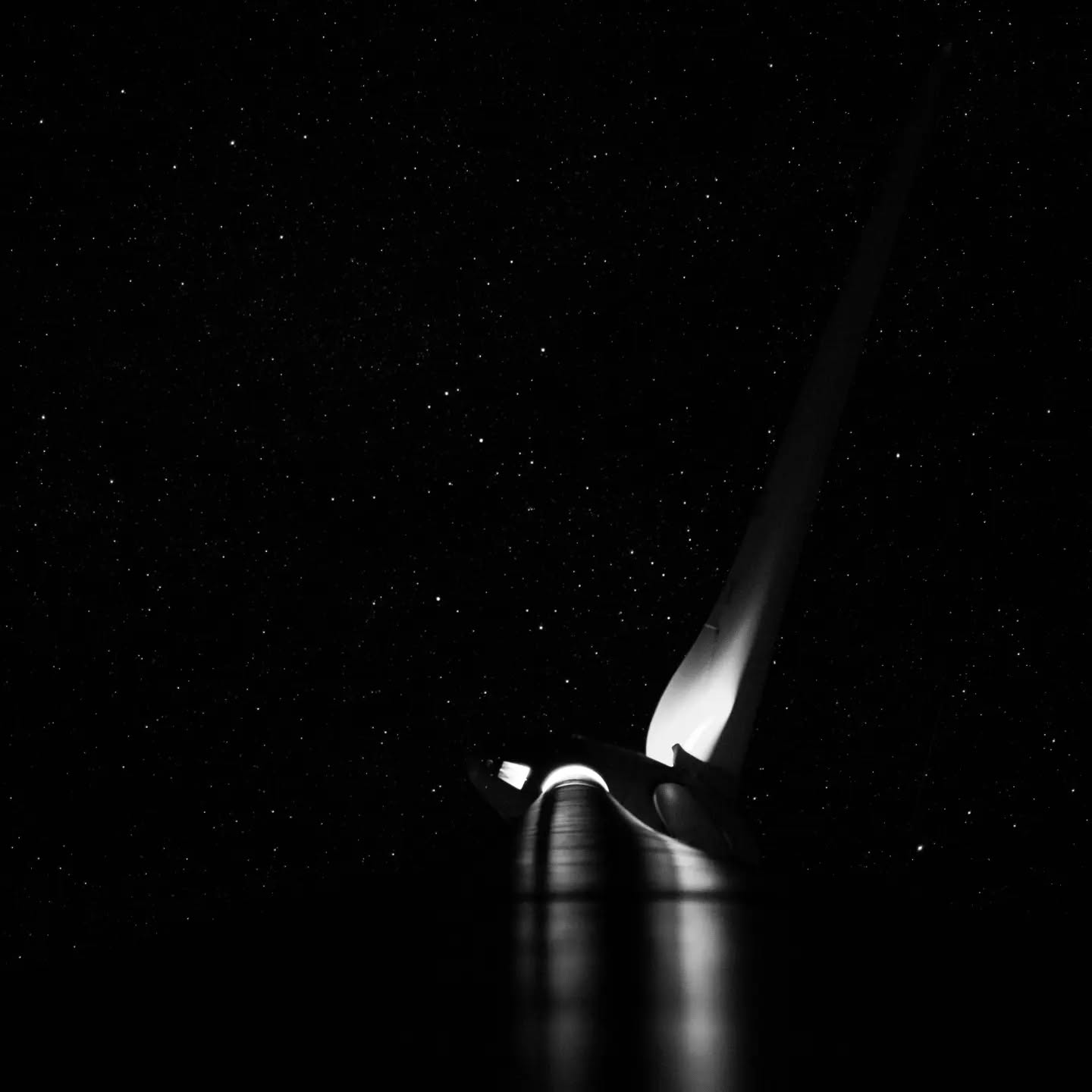 Black and white image of a spacecraft's nose cone lit against a dark, star-filled sky.