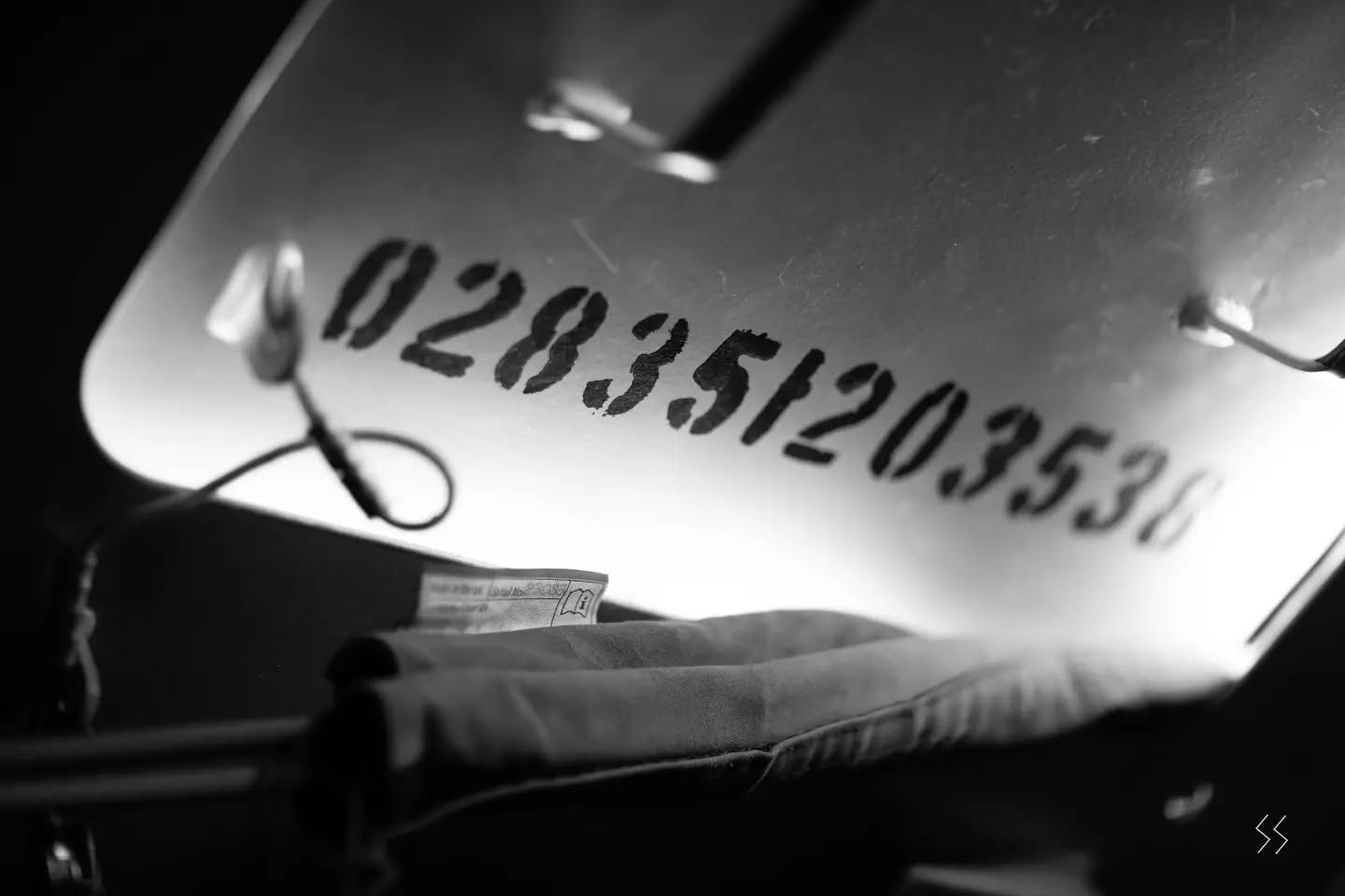 Black and white close-up of a stenciled serial number on a curved surface, with a folded cloth item below.