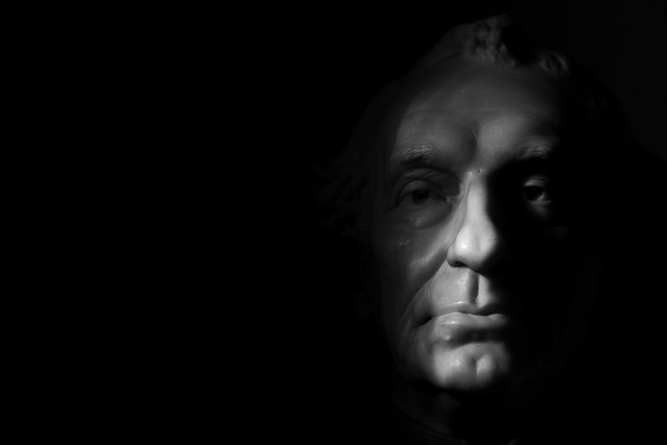 Black-and-white close-up of a man's face half-lit against a dark background, showing eyes, nose, and mouth in dramatic contrast.