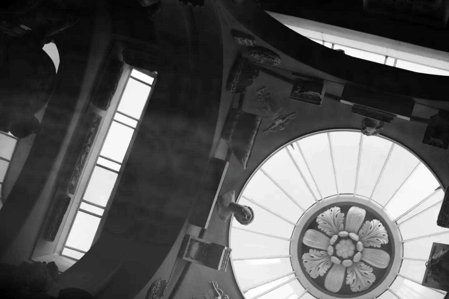 Black and white photo looking up at an ornate domed ceiling with a radial skylight and carved floral rosette medallion.