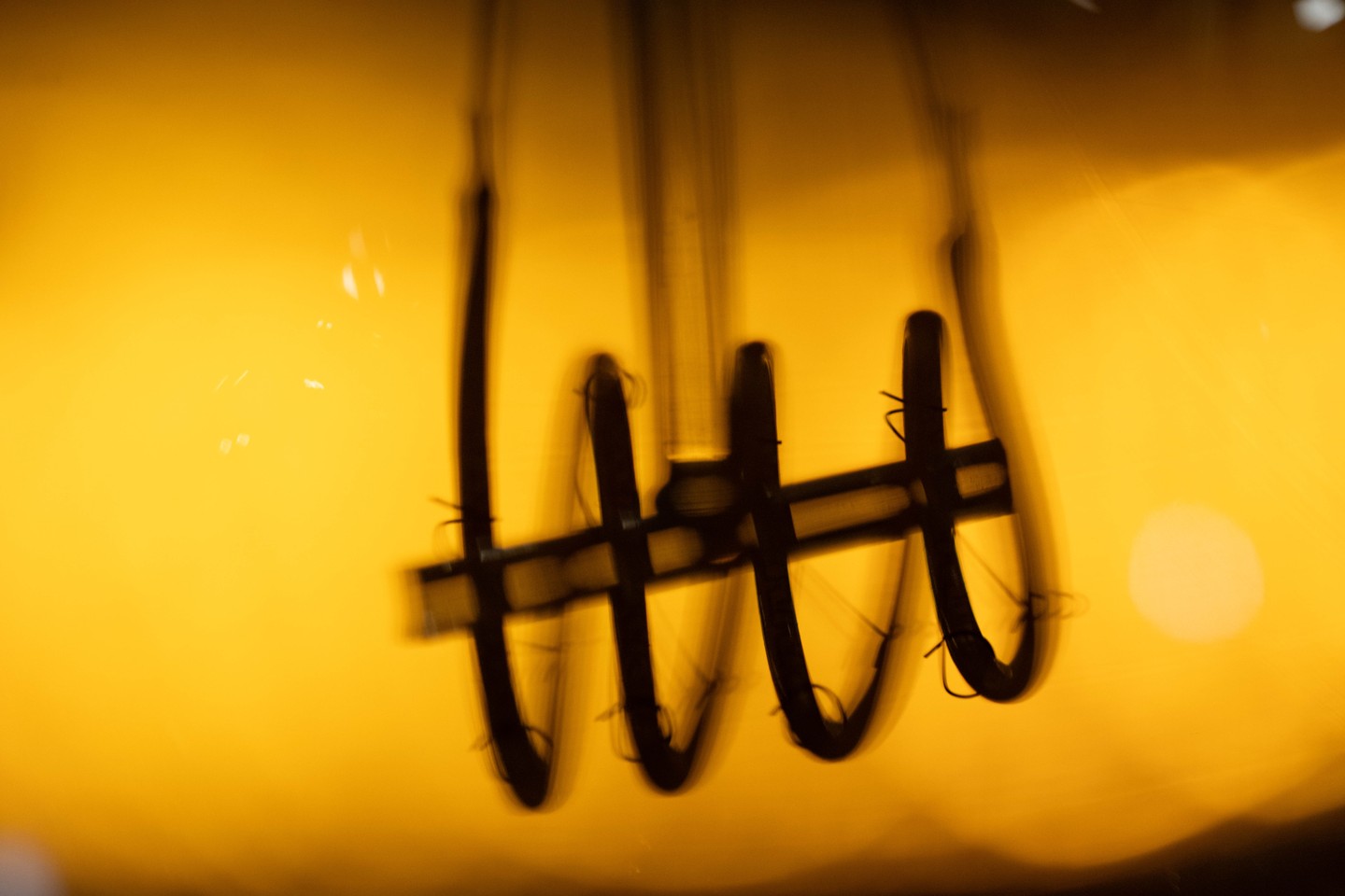 Blurred long-exposure image of a lightbulb filament, its wavy vertical wires glowing against an amber-yellow background.