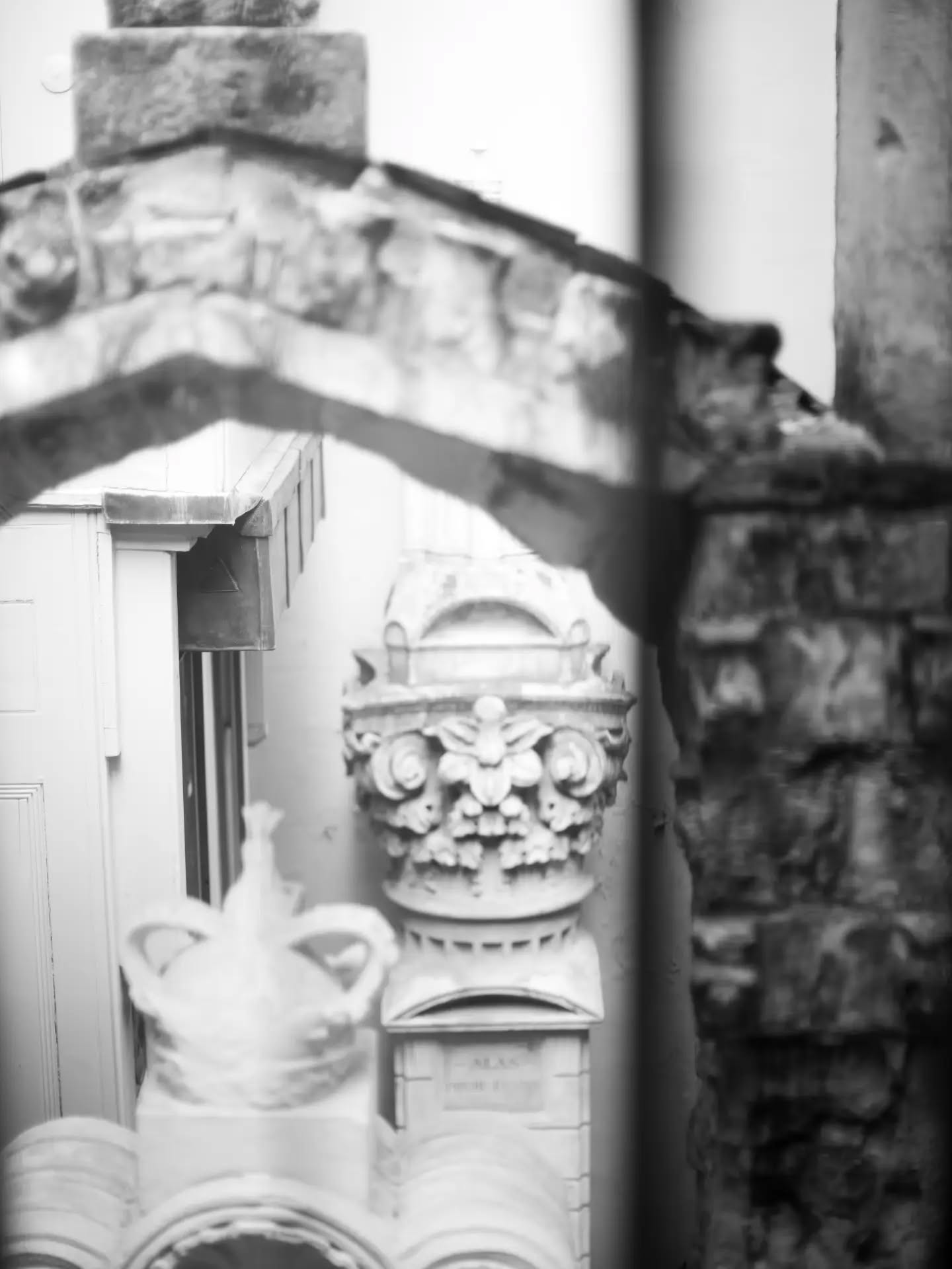 Black-and-white photo of ornate architectural stonework, including a carved capital with floral motifs, viewed through a wind