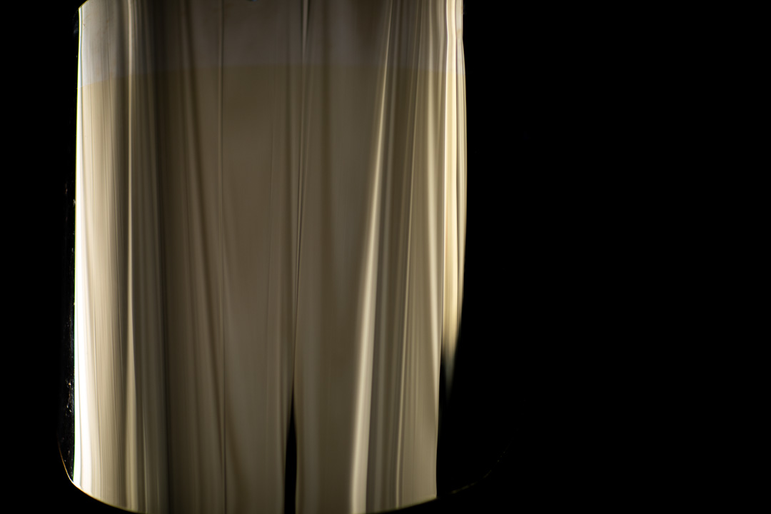 Vertically streaked fabric drapery lit centrally, with dark rounded edges fading to black on both sides.