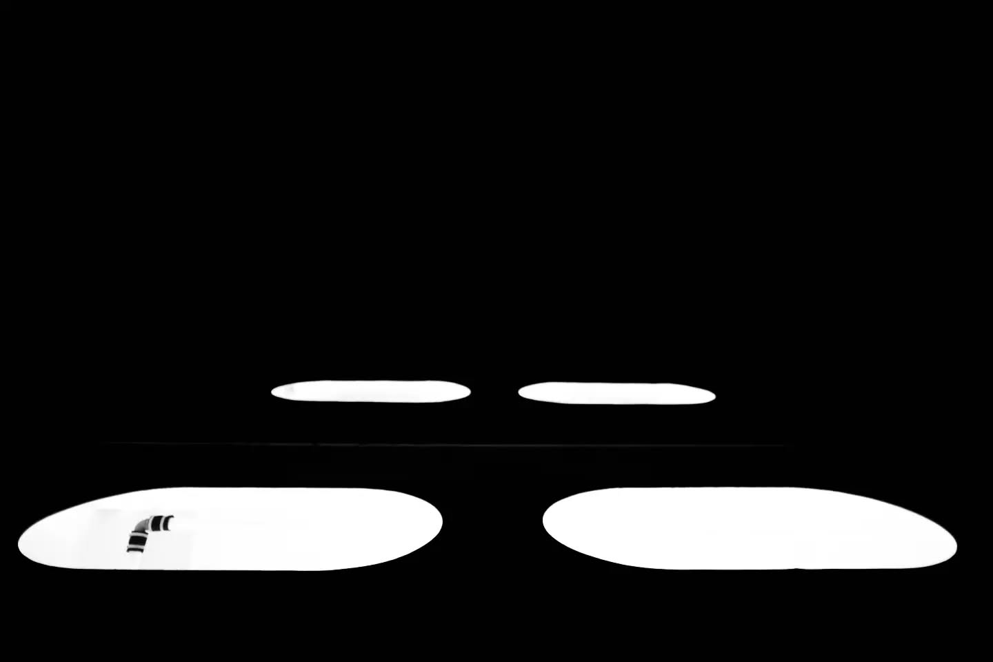 Four white surfboards arranged in two rows against a black background, reflections visible on the surfaces.