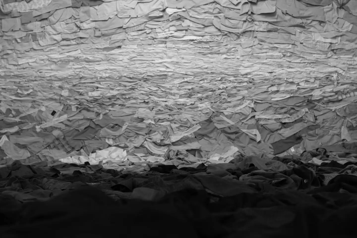 Black-and-white image of a textured surface covered in countless overlapping fabric scraps, brighter above, fading into dark 